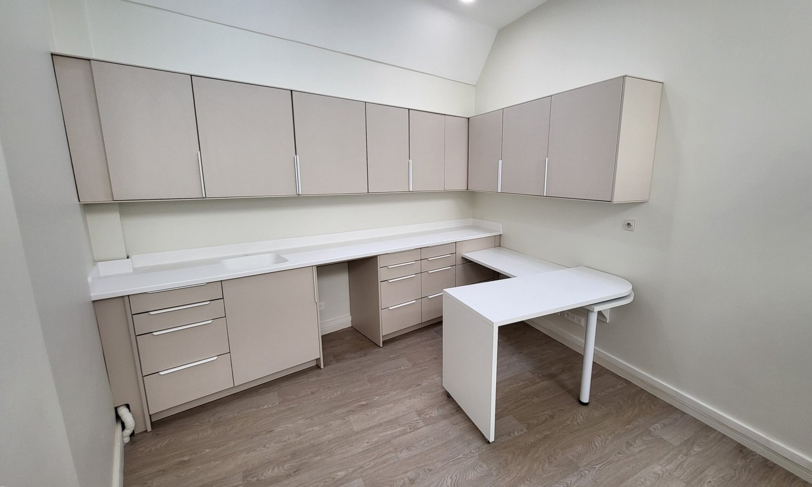 Aménagement sur mesure en L d’une salle de soins avec rangements hauts et plans de travail